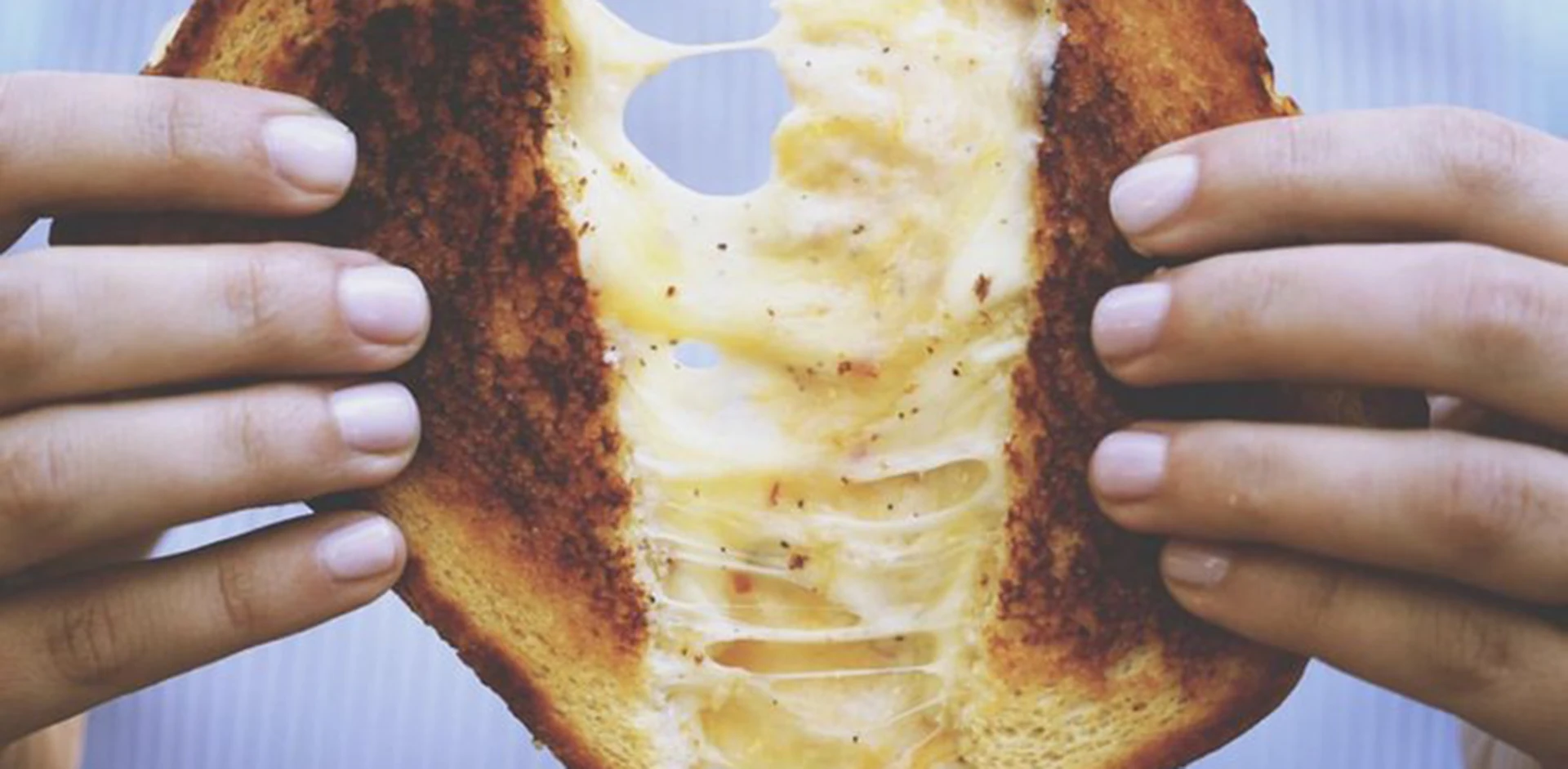 Close-up of hands opening a triple-decker grilled cheese sandwich